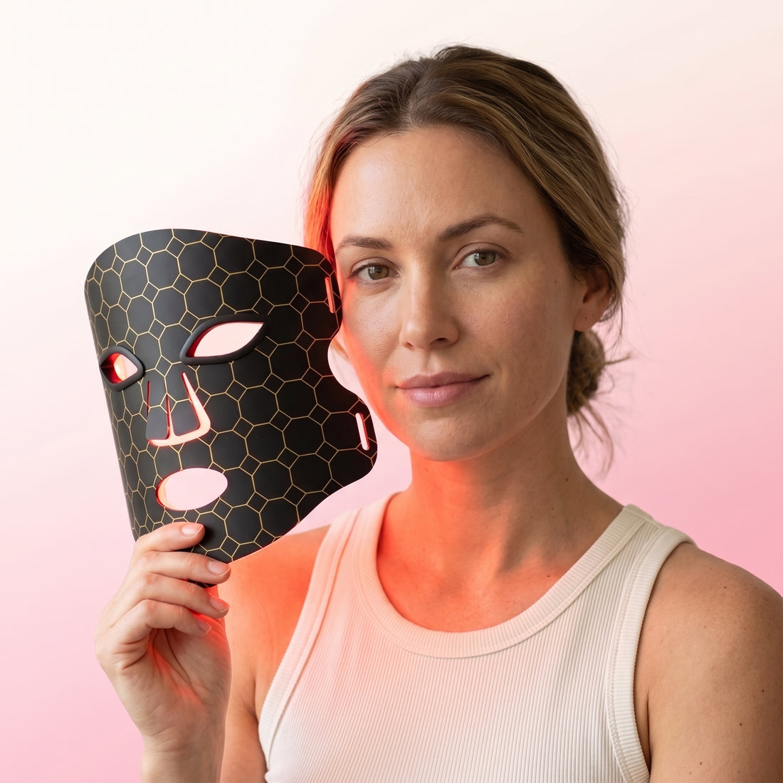 Woman holding the Lumina Pro LED light therapy mask glowing in red light mode beside her face