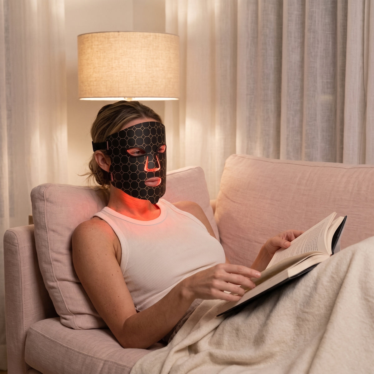 Evening | Woman wearing the Lumina Pro LED mask on a sofa in the evening, reading