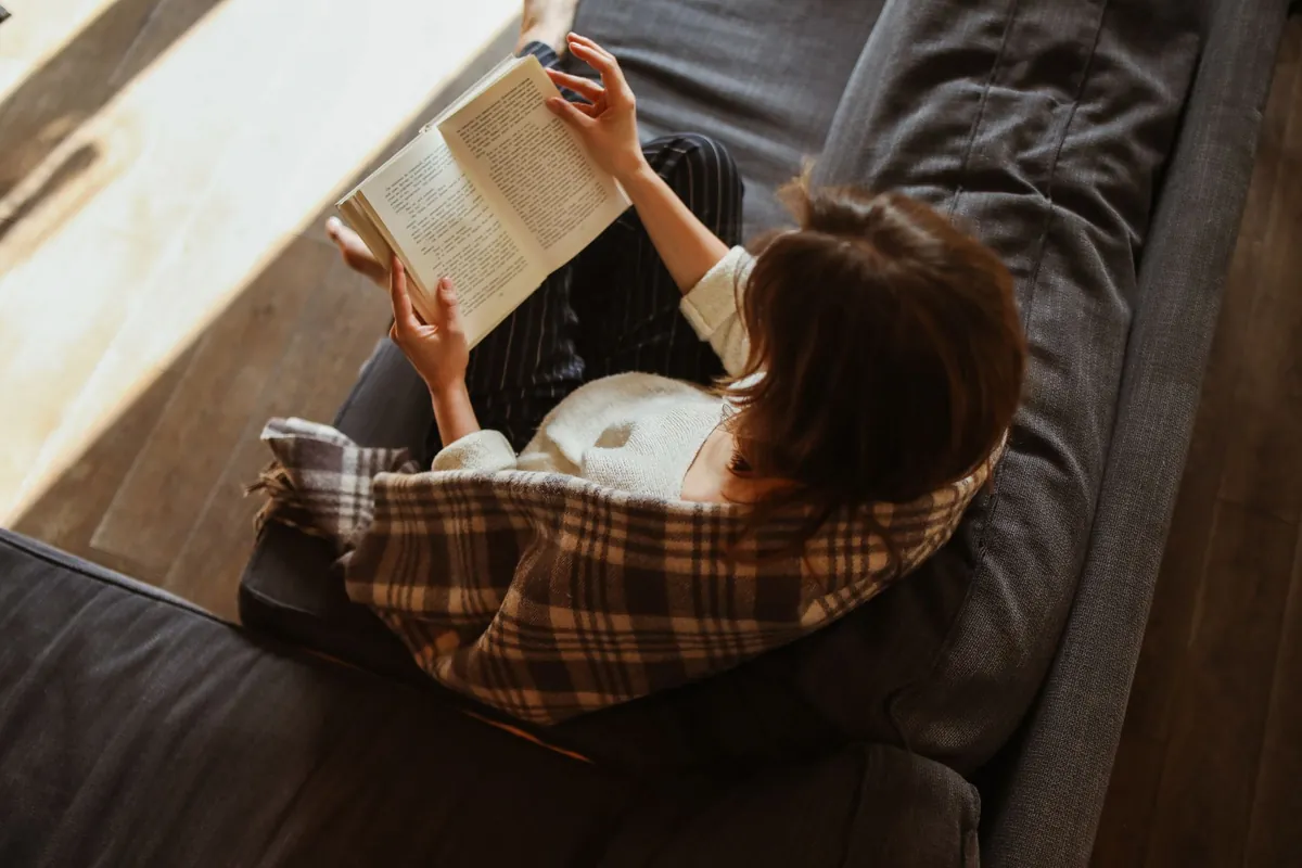 Woman reading on a sofa, wrapped in a blanket