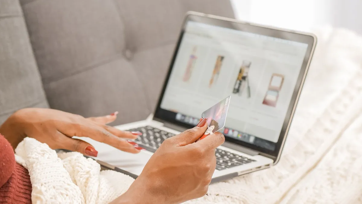 Woman on a couch holding a card while comparing options on her laptop