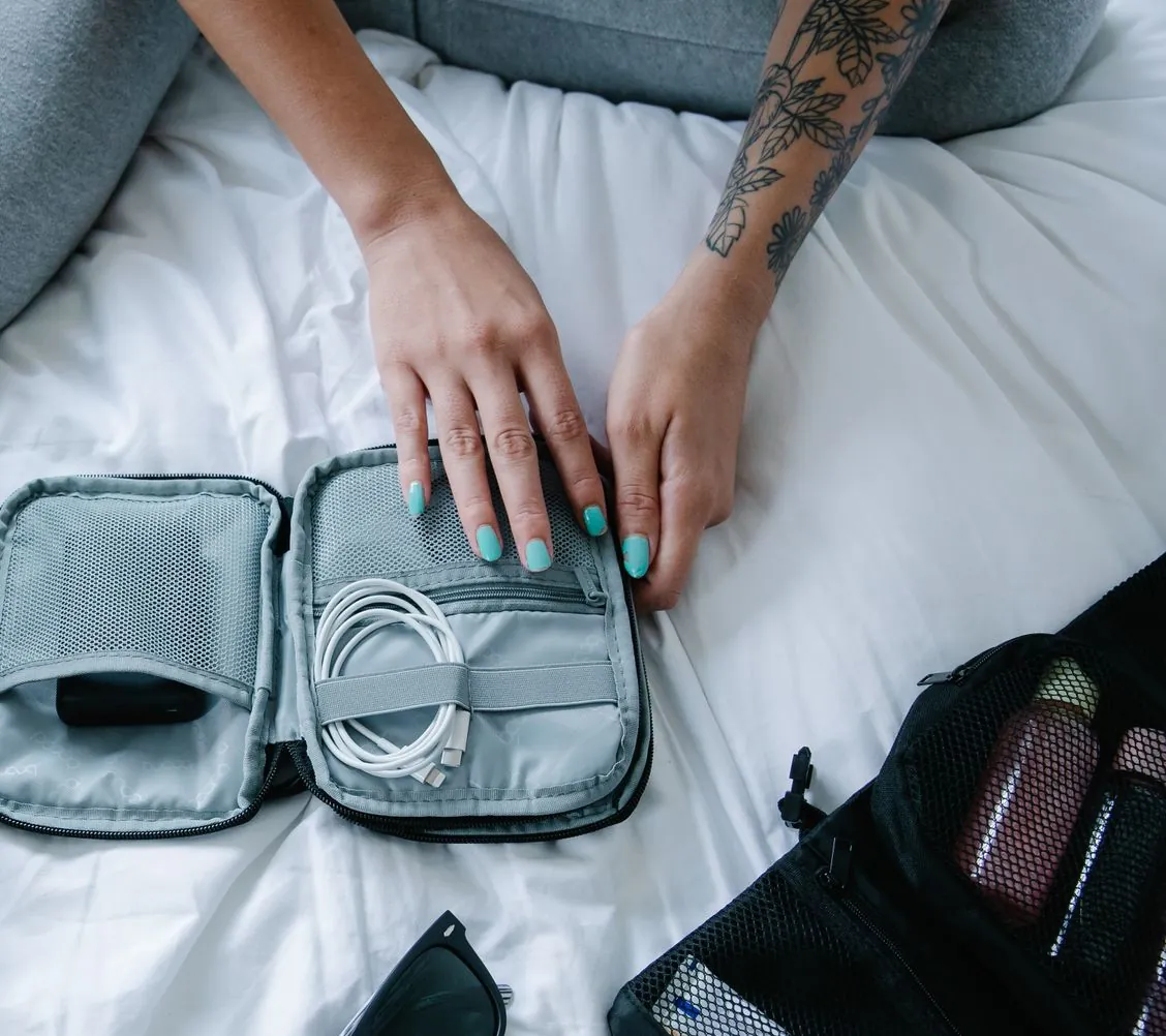 Hands packing a charger cable and electronics into a gray travel bag