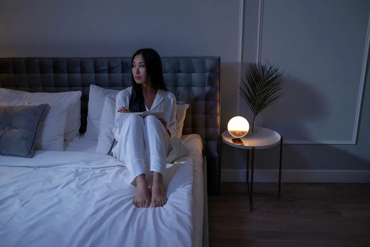 Woman in pajamas sitting on her bed in a softly lit bedroom