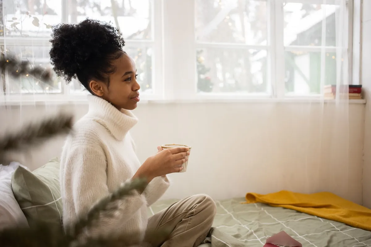 Woman enjoying a warm drink on her bed in the morning