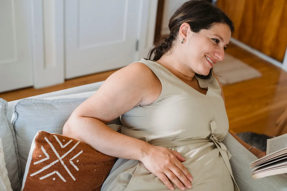 Pregnant woman smiling on a sofa with a book